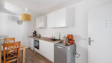A compact kitchen with white cabinets, a coffee machine, a kettle, and a small refrigerator.