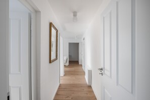 A hallway with white walls, wooden flooring, and doors on both sides.