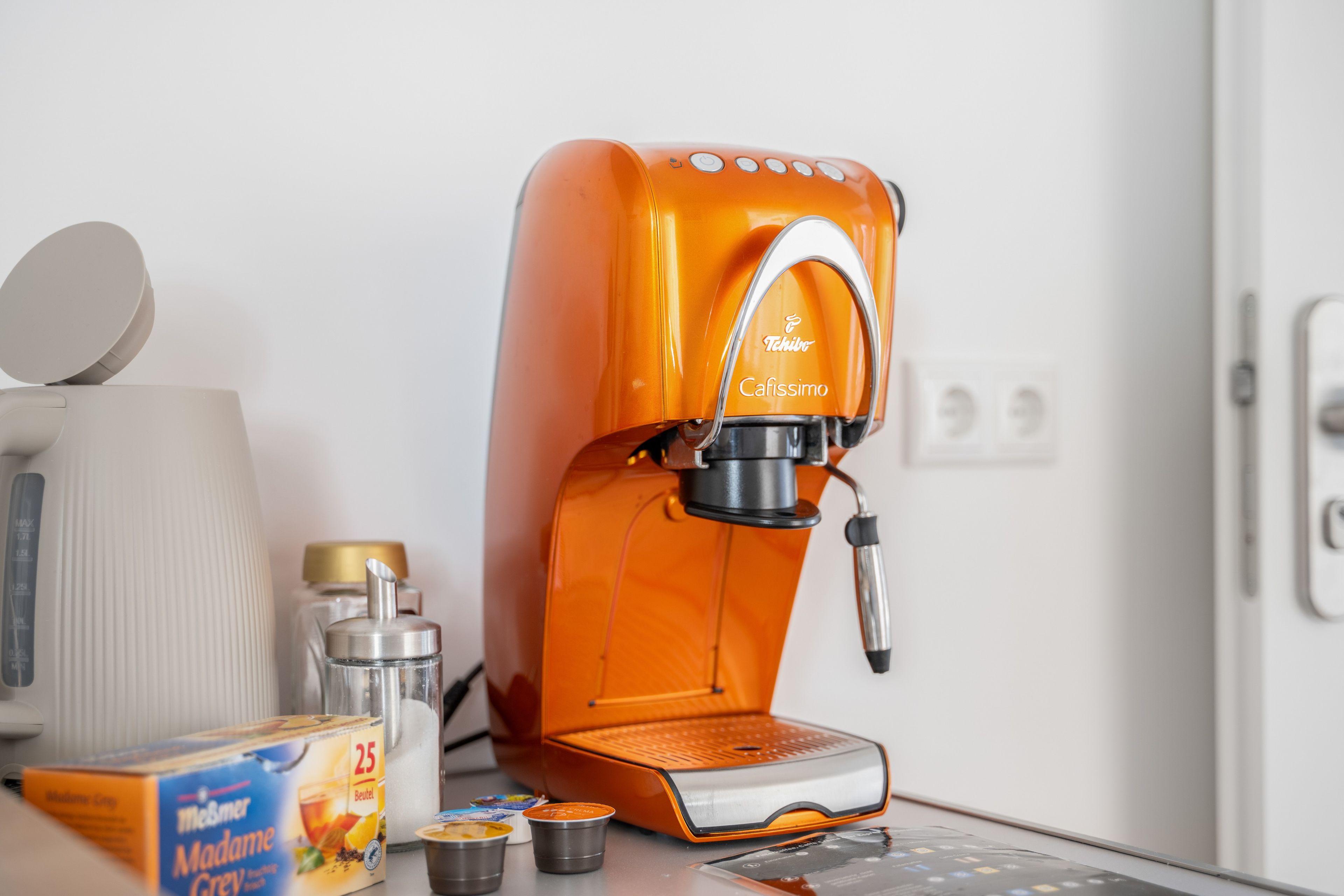 An orange coffee machine with a brand name, a box of tea, and a container of milk.