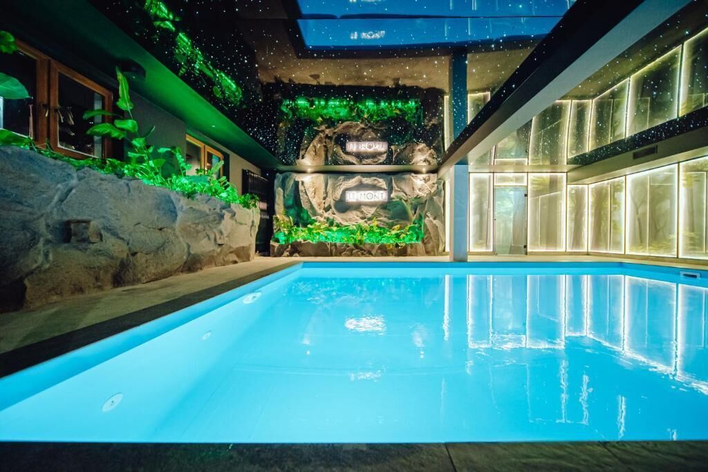Una piscina con parete rocciosa e vegetazione, interni moderni con pareti di vetro e un soffitto con luci simili a stelle.