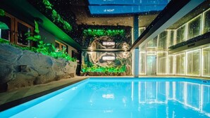 En swimmingpool med en klippevæg og grønt, et moderne interiør med glasvægge og et loft med stjernelignende lys.