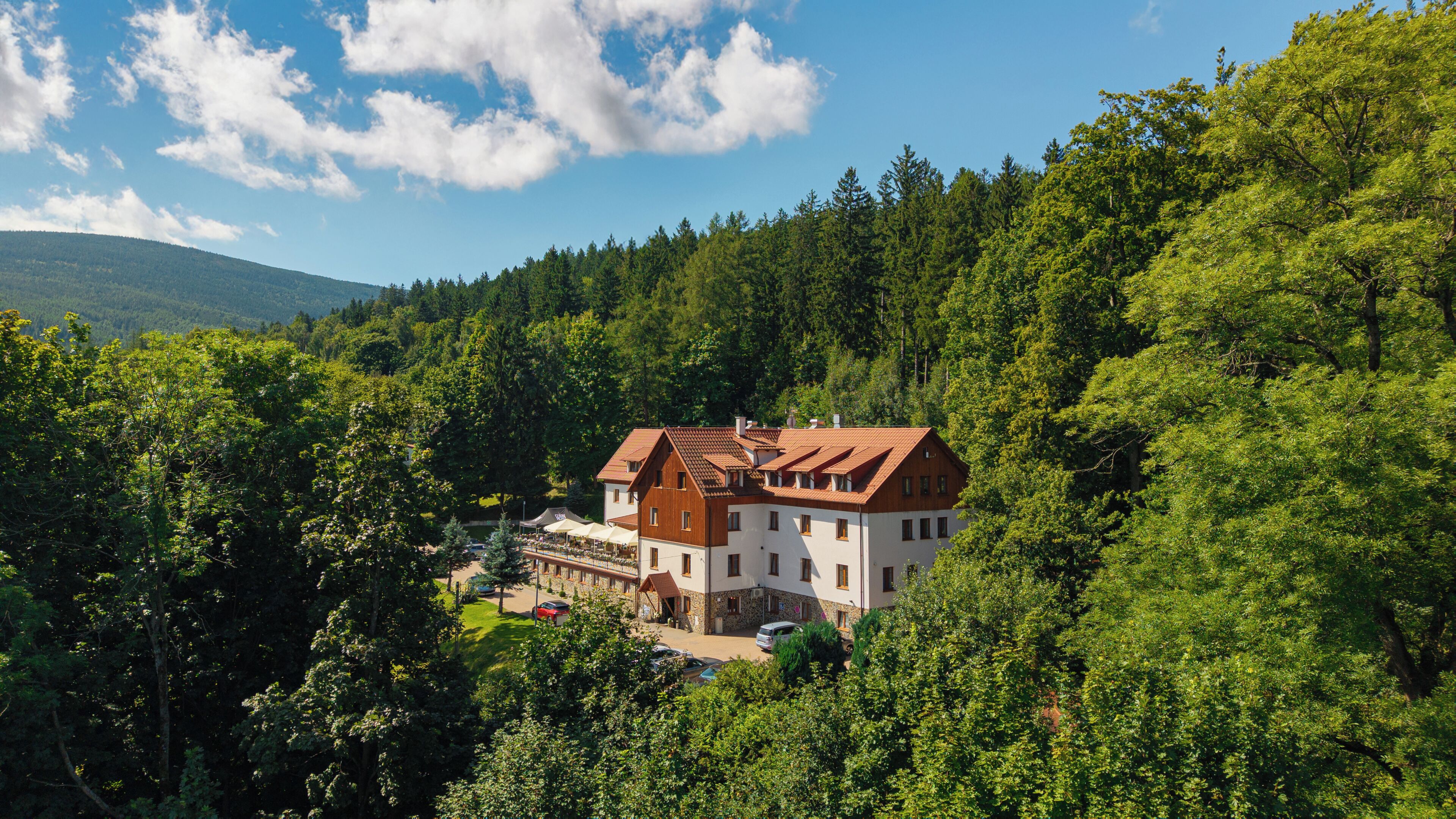 A two-story building with a red-tiled roof, surrounded by dense forest and hills.