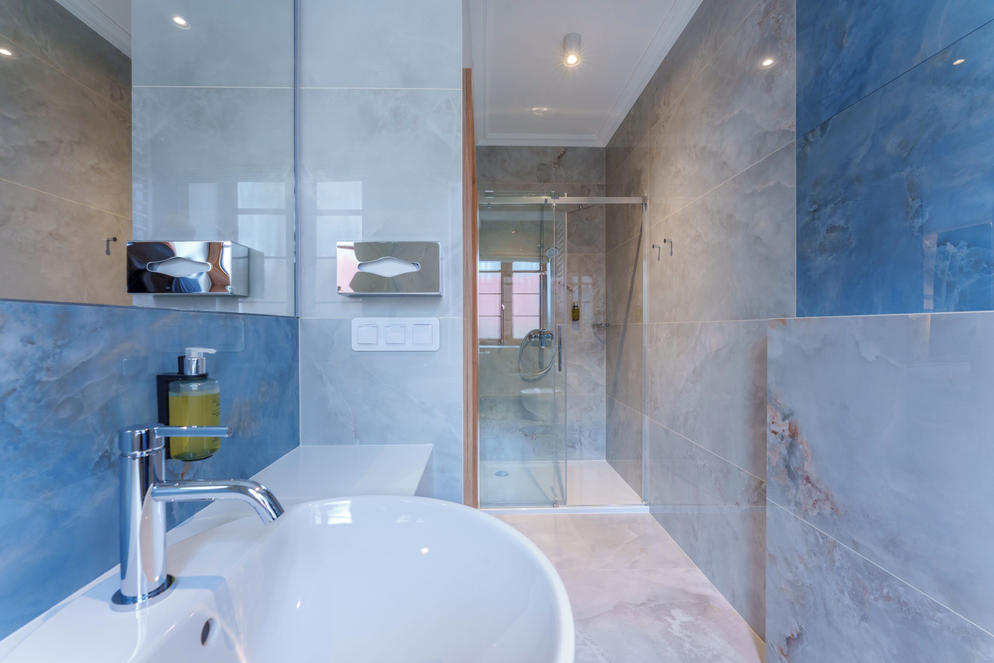 Un baño moderno con un lavabo blanco grande, una cabina de ducha de vidrio y paredes de mármol.
