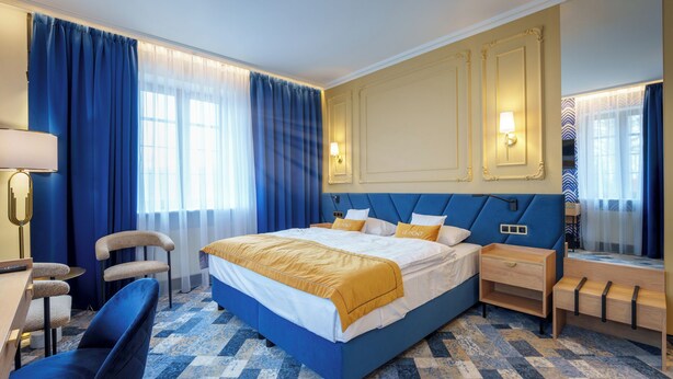 Et hotelværelse med en stor seng, et skrivebord, en stol og et spejl.