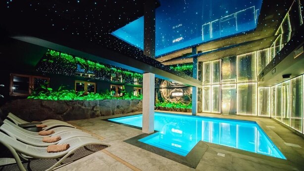 A modern indoor pool area with lounge chairs and a large digital screen displaying a starry sky.