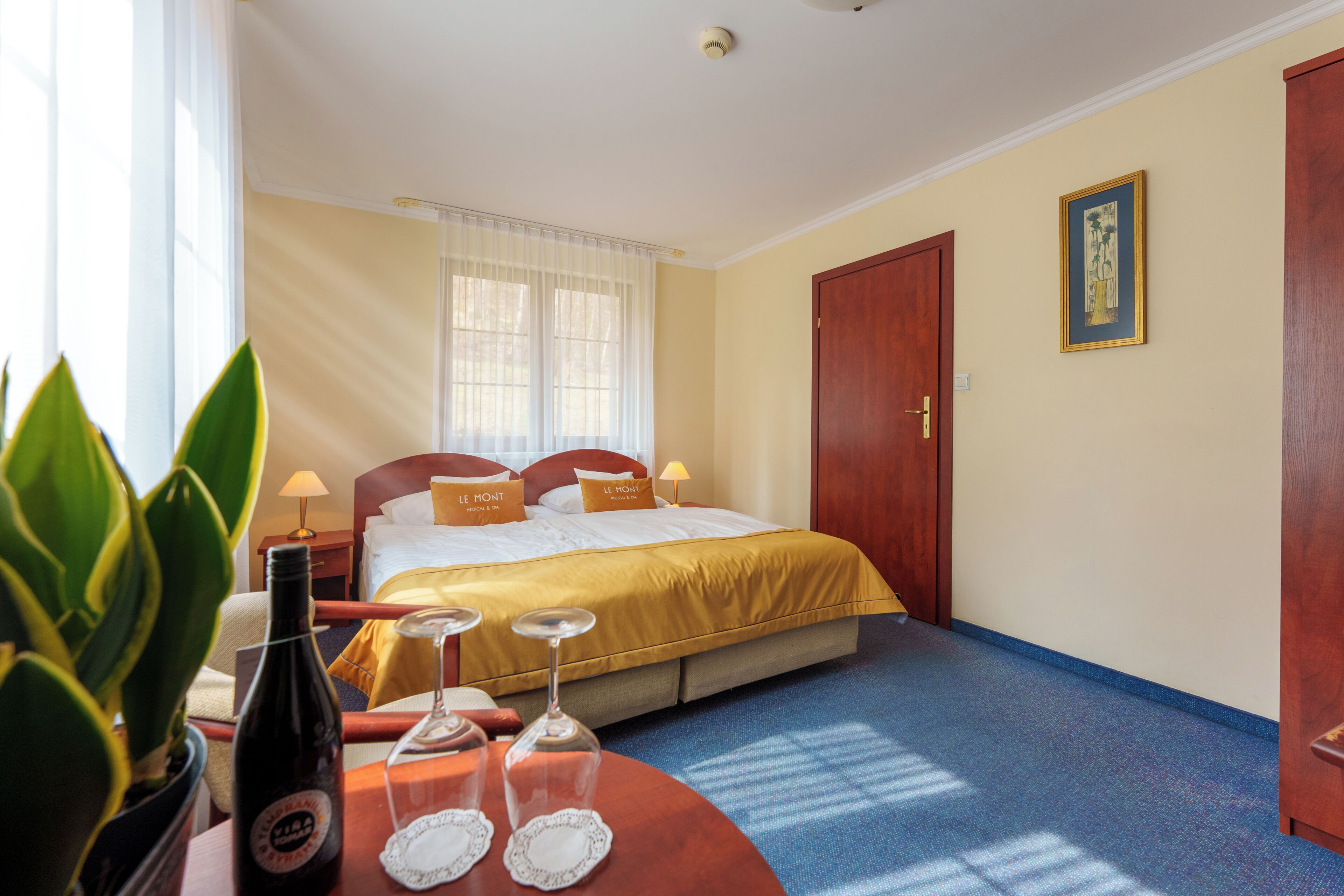 Una habitación de hotel con una cama, lámparas de noche, una botella y un vaso sobre una mesa.