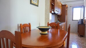 A dining area with a wooden table and chairs, a kitchen in the background, and a window with blinds. - Holiday house Casa Argelio (Vallehermoso)