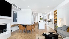 Ein modernes Wohnzimmer mit Kamin, ein Essbereich mit rundem Tisch und Stühlen sowie eine Küchenzeile mit Arbeitsfläche und Geräten.