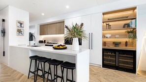A modern kitchen with a central island, bar stools, a wine rack, and a potted plant. - Eden at Kiama, penthouse apartment within Kove Apartments centrally located. (Kiama)
