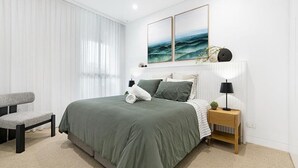 Ein modernes Schlafzimmer mit einem Bett, Nachttischen, einem Sessel und Kunstwerken an der Wand.