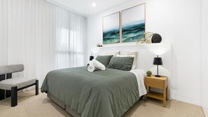 Ein modernes Schlafzimmer mit einem Bett, Nachttischen, einem Sessel und Kunstwerken an der Wand.