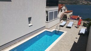 Ein rechteckiger Swimmingpool mit klarem, blauem Wasser neben einem Gebäude mit einem Balkon.