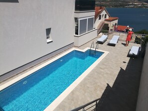 Ein rechteckiger Swimmingpool mit klarem, blauem Wasser neben einem Gebäude mit einem Balkon.