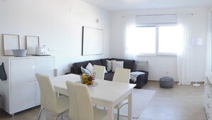 Ein modernes Wohnzimmer mit einem weißen Esstisch, einer Couch und einem Fenster mit Vorhängen.