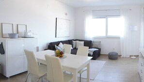 Ein modernes Wohnzimmer mit einem weißen Esstisch, einer Couch und einem Fenster mit Vorhängen.