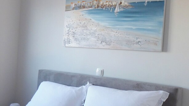 Ein Schlafzimmer mit einem Bett, zwei Kissen, einem Nachttisch und einem Bild einer Strandansicht an der Wand.