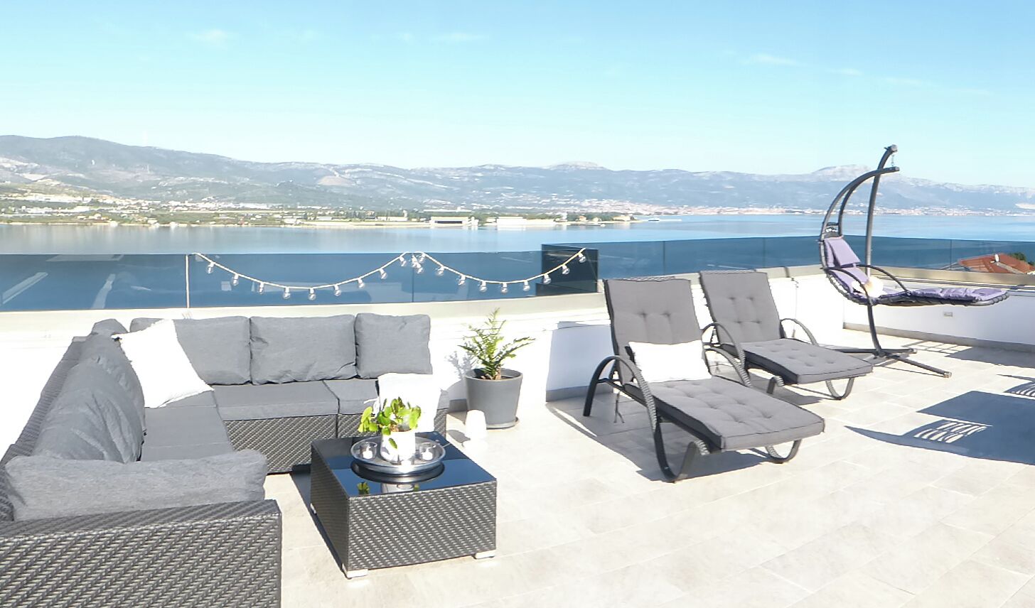A rooftop terrace with a sofa set, lounge chairs, and a potted plant.