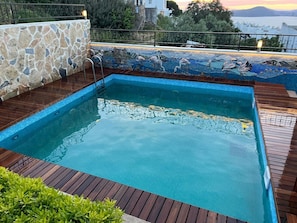 En swimmingpool med en mur av sten och ett trädäck, omgiven av ett räcke och med utsikt över havet.