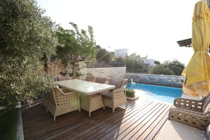A wooden deck with outdoor furniture, a swimming pool, and a stone wall.