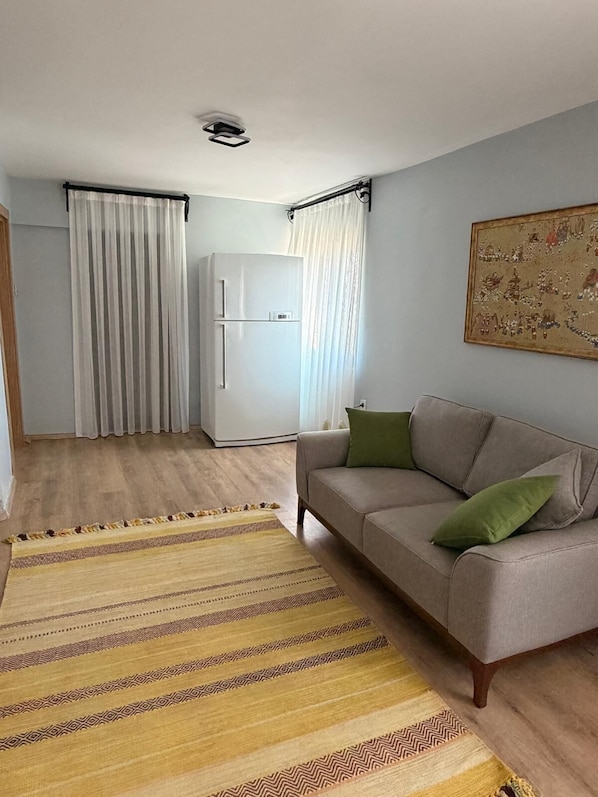 A living room with a sofa, a patterned rug, a white refrigerator, and a painting on the wall.