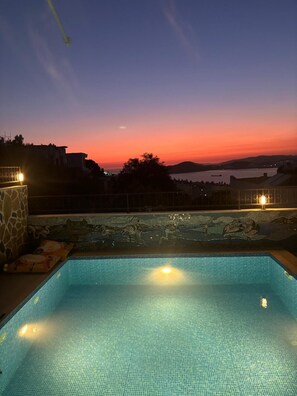 A swimming pool with a view of a sunset and distant hills.