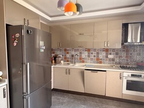 A modern kitchen with a stainless steel refrigerator, beige cabinets, a patterned backsplash, and a gas stove.