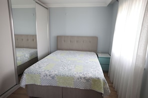A bedroom with a bed, a nightstand, a mirror, and a window with curtains.