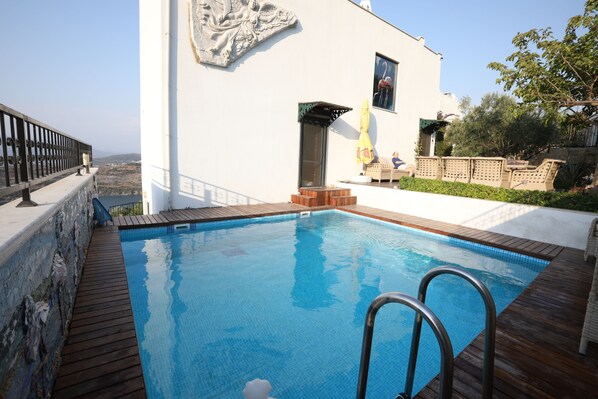 A swimming pool with a wooden deck, a white building with a mural, and a view of the landscape.