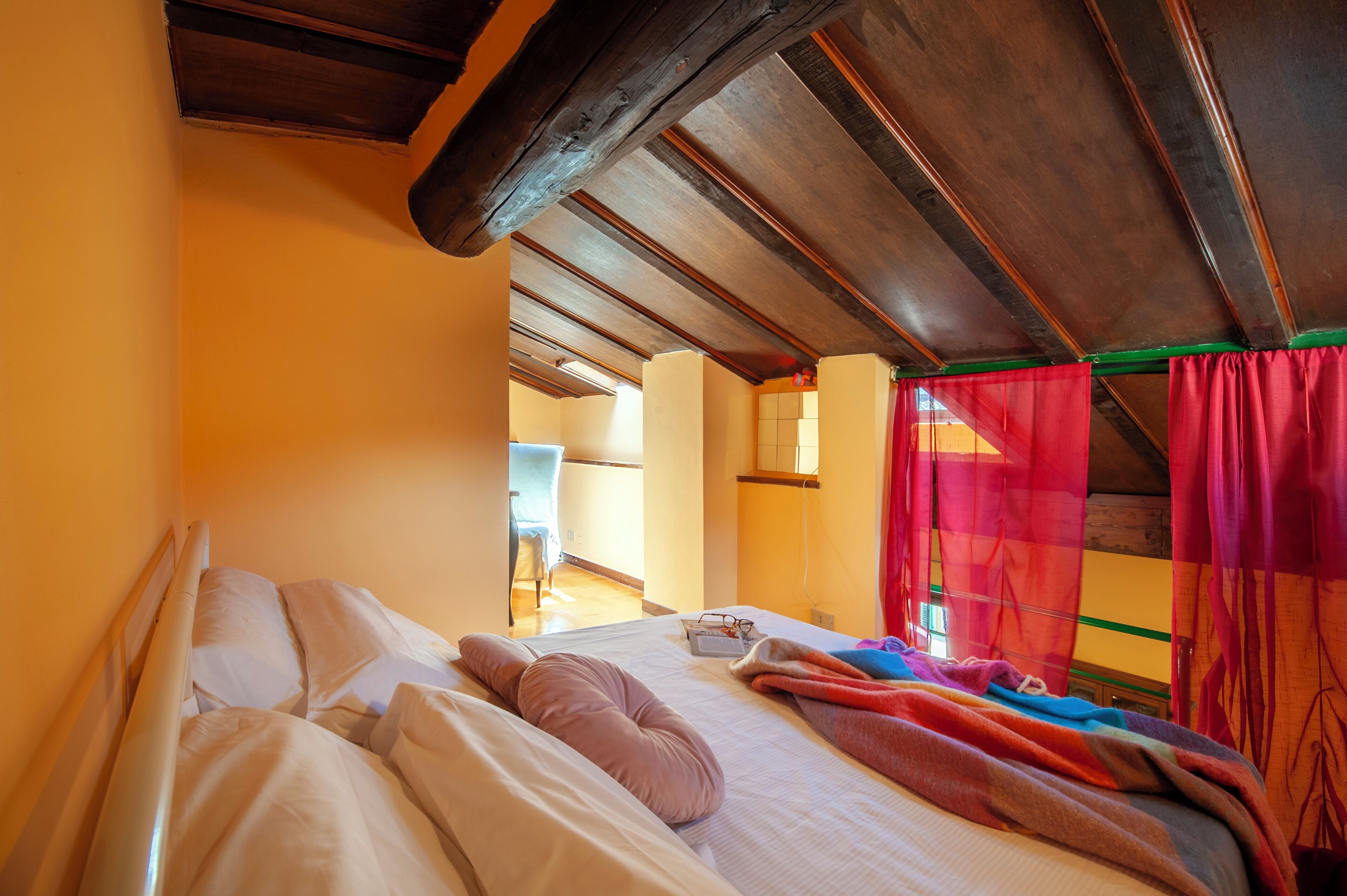 A room with a bed, a window with a red curtain, and a wooden ceiling.