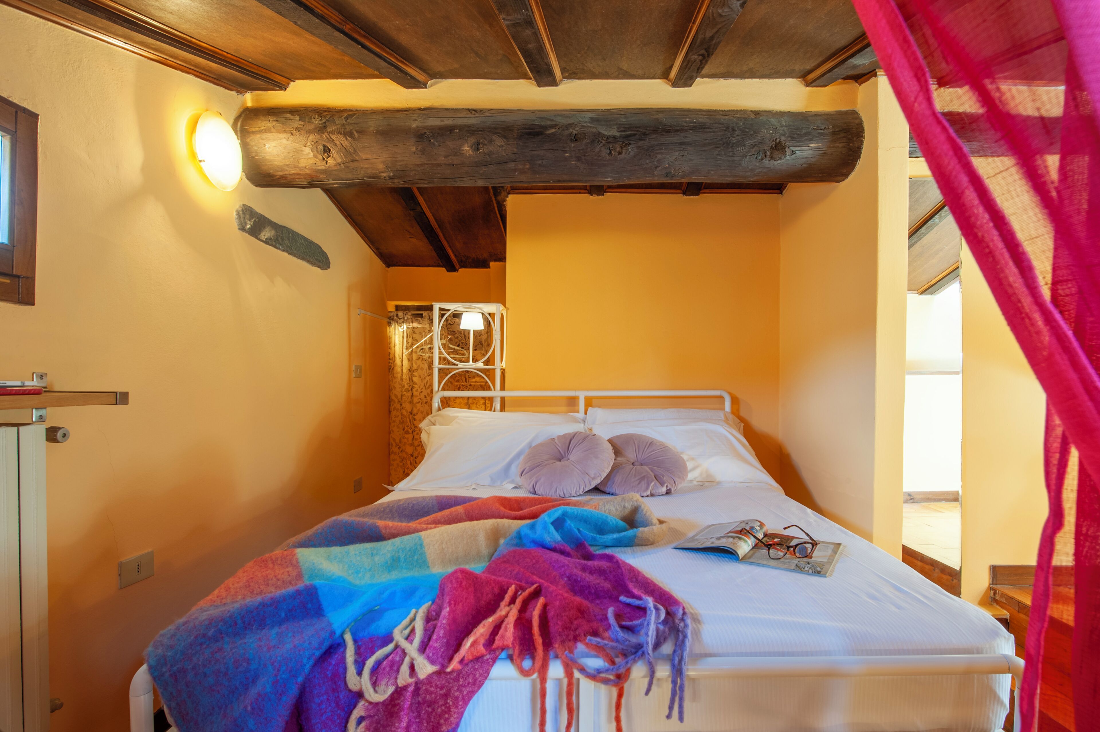 Un letto con una coperta colorata, un comodino e una finestra con tende.