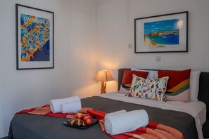 Une chambre d’hôtel comprenant un lit, une table de chevet, une lampe, une carte encadrée de Limassol et un tableau encadré représentant Chypre.