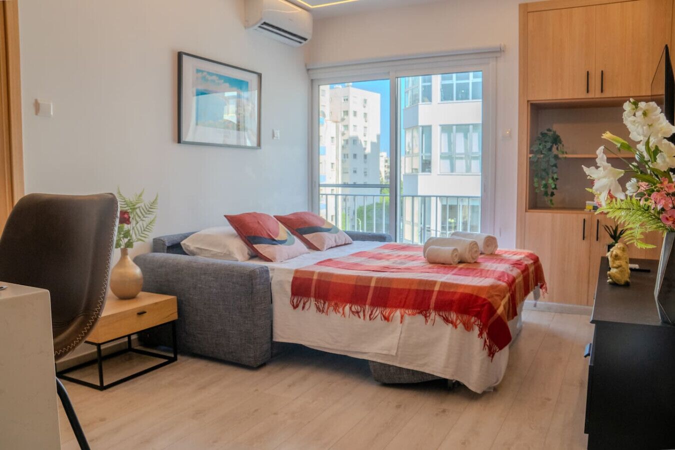 Une chambre à coucher avec un lit, un bureau, une chaise, une fenêtre et une vue sur des immeubles.