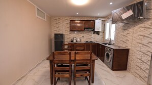 A compact kitchen with a dining table, chairs, a washing machine, and a built-in oven.