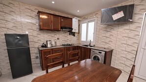 A kitchen with a dining table, wooden cabinets, a washing machine, and a black refrigerator.