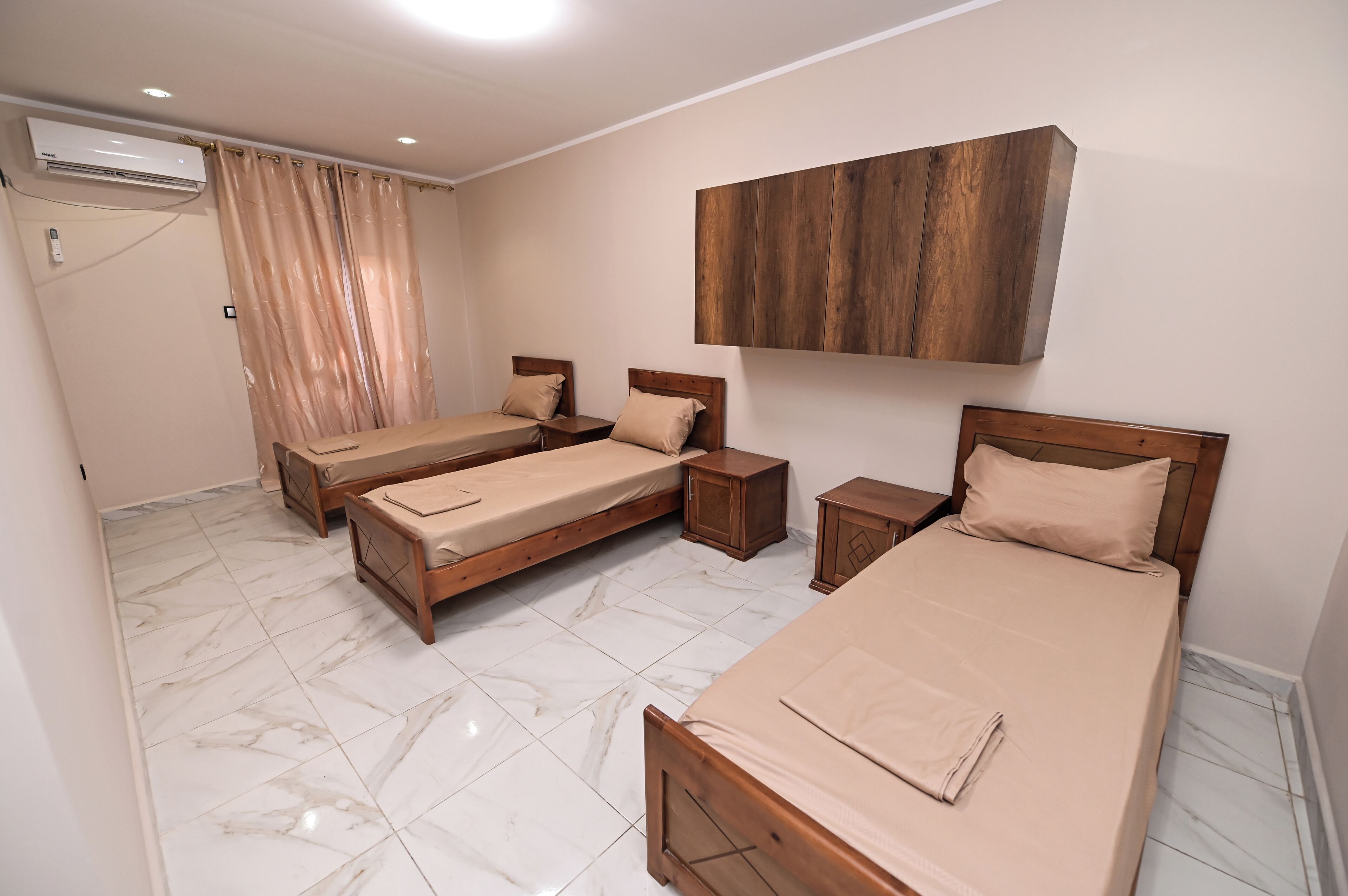 A hotel room with two single beds, a wooden headboard, a marble floor, an air conditioning unit, and a wooden cabinet.