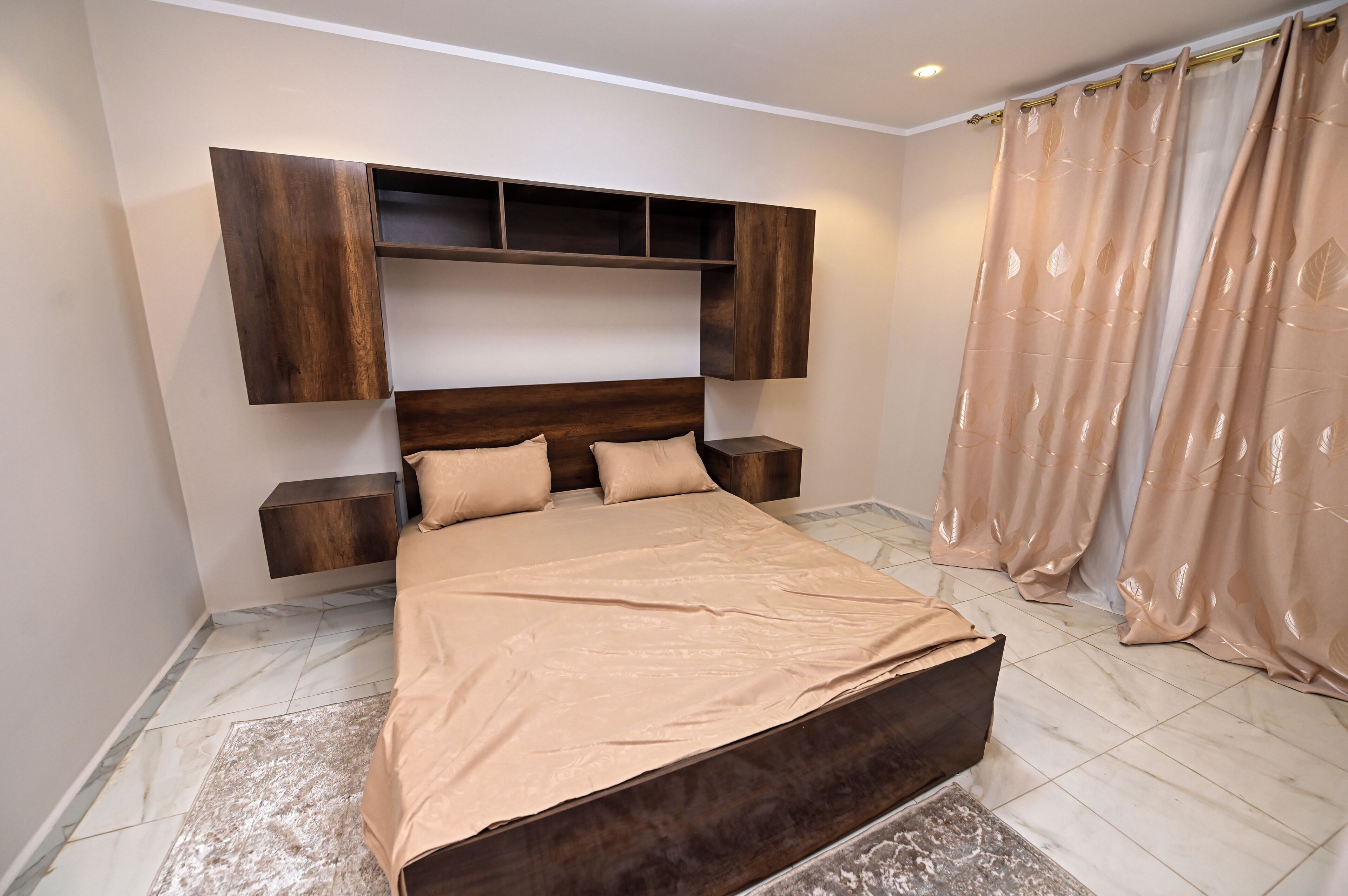 Une chambre à coucher avec un lit, une tête de lit en bois, des tables de chevet et un rideau.