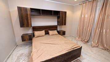 Une chambre à coucher avec un lit, une tête de lit en bois, des tables de chevet et un rideau.