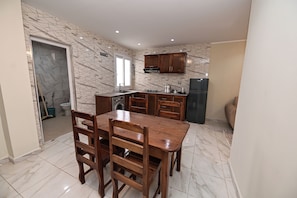 A modern kitchen with a dining area, featuring a marble backsplash, wooden cabinets, and a built-in oven. - Hostel Bouhcair (Jijel)