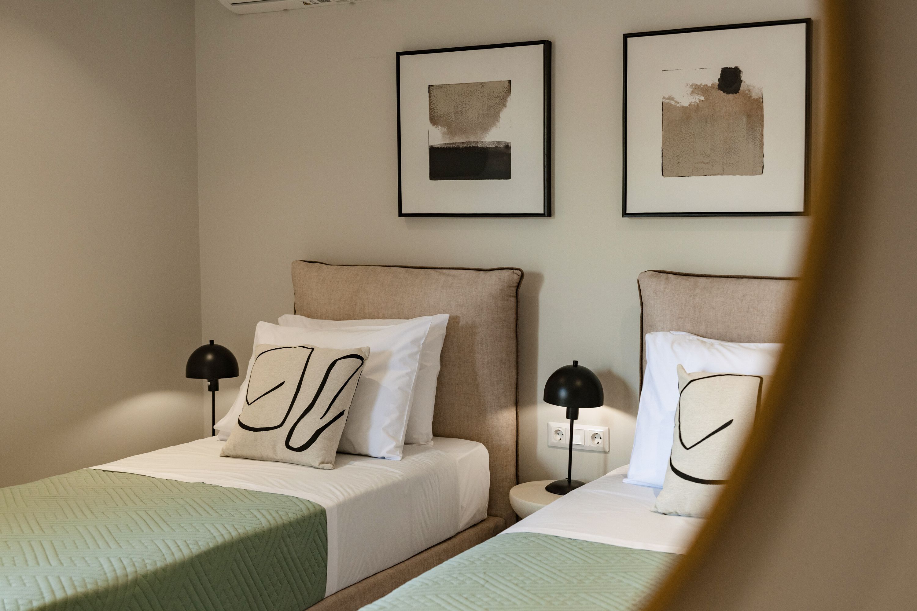Une chambre d’hôtel avec deux lits, chacun étant équipé d’un oreiller et d’une lampe. Deux tableaux encadrés sont accrochés au mur, au-dessus des lits.