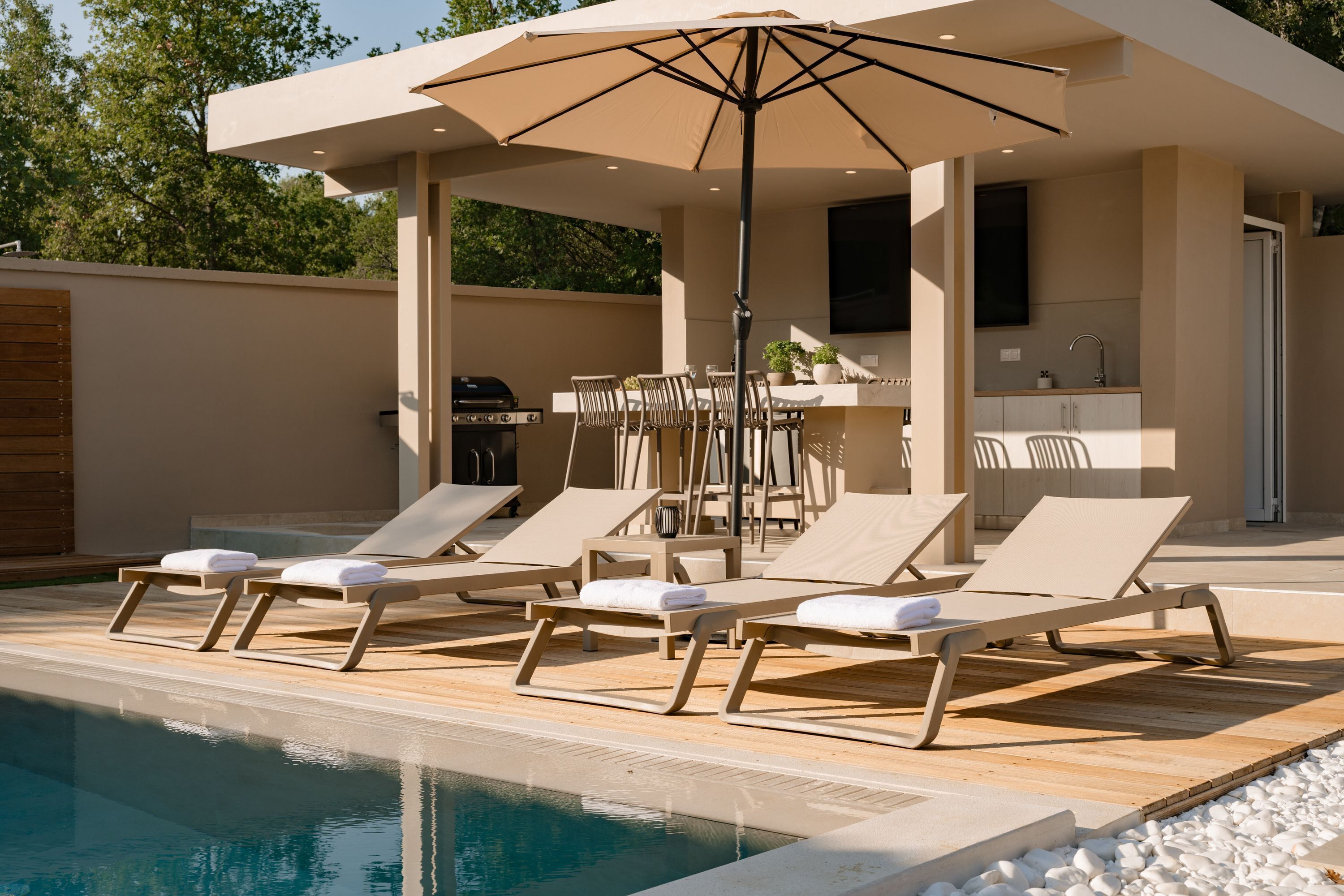 Ein Poolbereich mit Liegestühlen, einem Sonnenschirm, einem Grill und einer Küchenzeile.