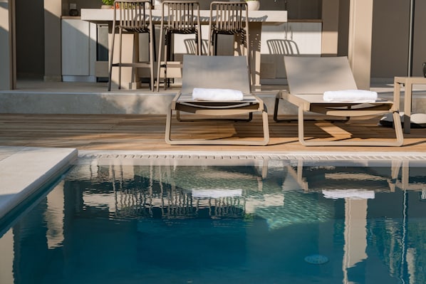 Zona de piscina con sillas de descanso y una mesa, con vista despejada a la piscina.