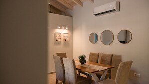 A dining area with a wooden table, four chairs, and a vase with flowers. There are two framed pictures on the wall and an air conditioning unit above the table. - Villa Idola Dassia Corfu (Corfu)
