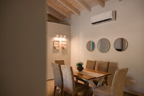 A dining area with a wooden table, four chairs, and a vase with flowers. There are two framed pictures on the wall and an air conditioning unit above the table. - Villa Idola Dassia Corfu (Corfu)