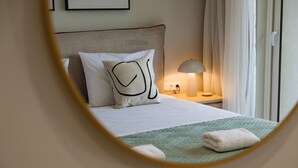 A neatly made bed with a green quilt, a white pillow with a black design, and a bedside lamp on a wooden nightstand. - Villa Idola Dassia Corfu (Corfu)