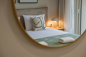 A neatly made bed with a green quilt, a white pillow with a black design, and a bedside lamp on a wooden nightstand. - Villa Idola Dassia Corfu (Corfu)