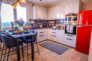 A modern kitchen with white cabinets, a red refrigerator, and a dining area with a table set for two. - 4.97 Super Host`s New Boutique & Prime Location (Limassol)