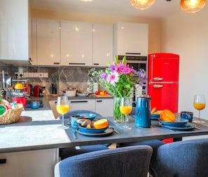 A modern kitchen with white cabinets, a red refrigerator, and a dining area with blue tableware. - 4.97 Super Host`s New Boutique & Prime Location (Limassol)