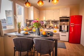 Una cocina moderna con una isla central, dos taburetes de bar, un refrigerador rojo y una mesa de comedor lista para el desayuno.
