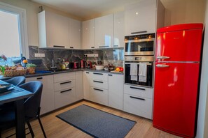 Une cuisine moderne avec des meubles blancs, un réfrigérateur rouge et un four encastré.