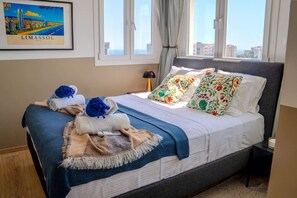 Una cama bien hecha con colcha azul y blanca, almohadas florales y un cuadro enmarcado con una vista urbana.